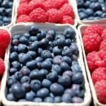 Close-up of ripe blueberries and raspberries in market baskets, showcasing fresh summer fruits.