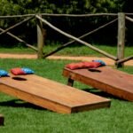 Wooden cornhole boards with colorful bean bags on a green lawn during a sunny day outdoors.